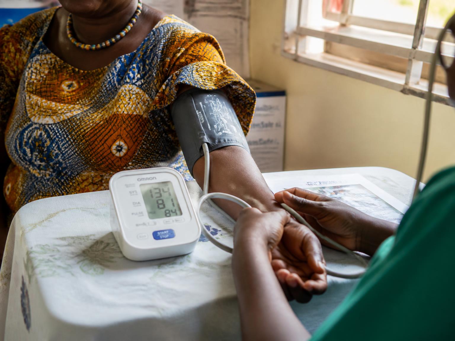 A health worker measuring a woman's blood pressure with a digital arm cuff at a clinic table
