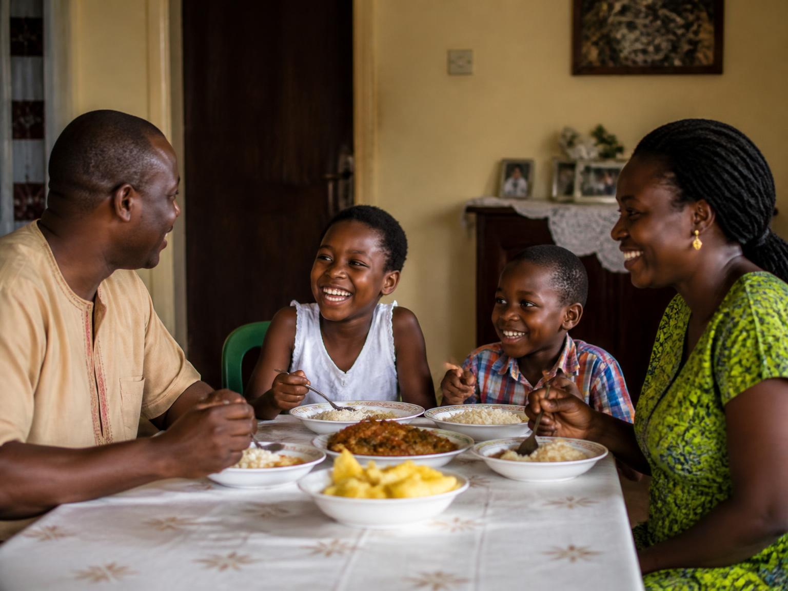 A family of four sharing bowls of rice and stew around the table at home, laughing