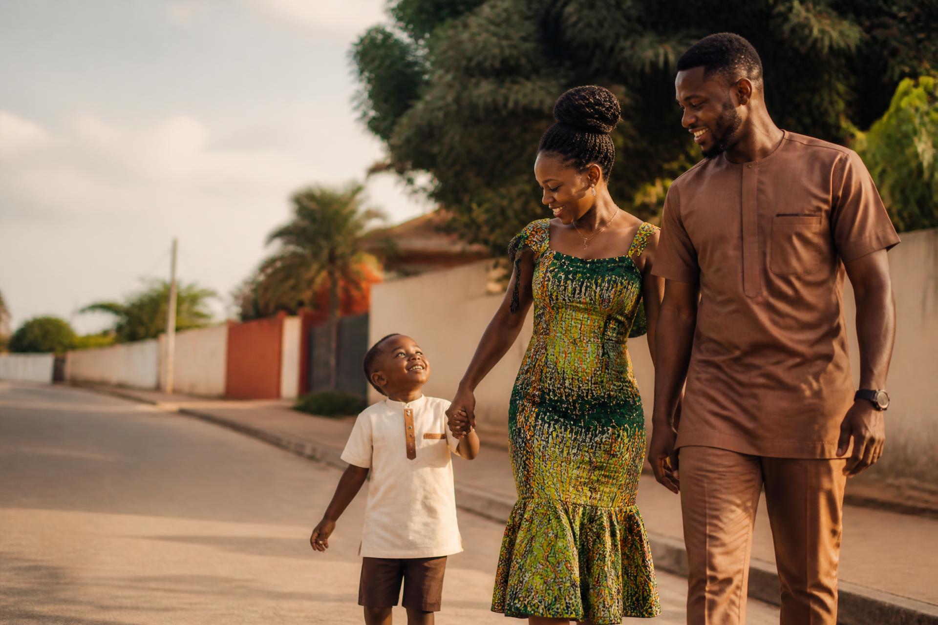A Ghanaian mother, father and young son walking together along a neighbourhood street at sunset