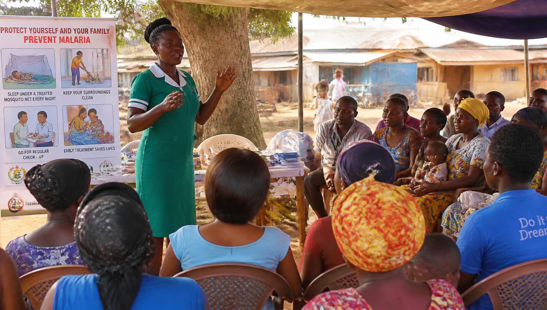 A nurse leading an open-air community health education session for a seated group