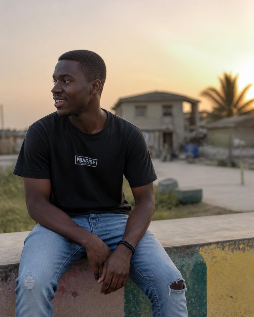 A young Ghanaian man sitting on a low wall outdoors at golden hour
