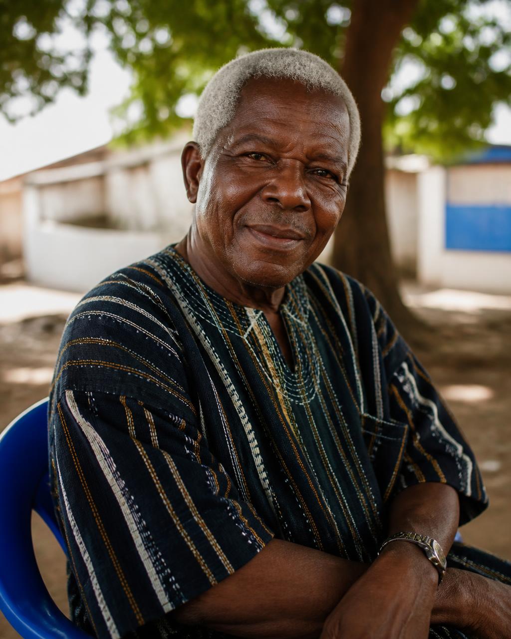 An older Ghanaian man in woven cloth sitting in the shade of a tree